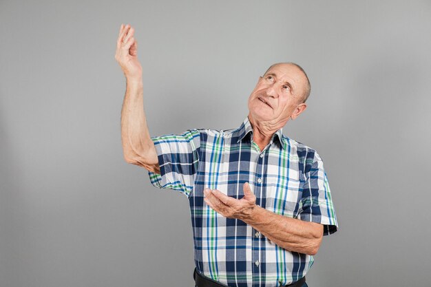 Пожилой человек указывает в сторону. Серьезный зрелый мужчина, указывающий пальцем в сторону, на сером фоне, копирует пространство.