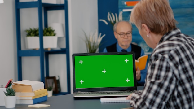 Persona anziana che legge su schermo verde, mock up, display chroma key del laptop, scrive su notebook che lavora da casa. donna anziana che guarda al pc con desktop isolato, mentre l'uomo è seduto sul divano