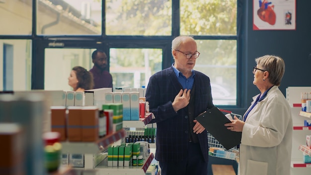 Photo elderly person with heartache talking to pharmacist about cardiology pills, having cardiac problem and heartburn in drugstore. client with chest pain and cardiovascular pressure asking for medicine.