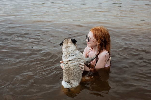 Elderly pug bathing in the river with a little girl