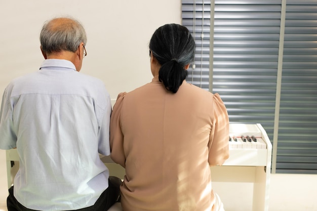 Elderly senior couple play Piano music together Group of Two Asian smart mature Person retire and get pension fund Grandparent express feeling happy treatment Concept grow old together copy space