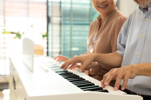 Elderly senior couple play piano music together group of two\
asian smart mature person retire and get pension fund grandparent\
express feeling happy treatment concept grow old together copy\
space