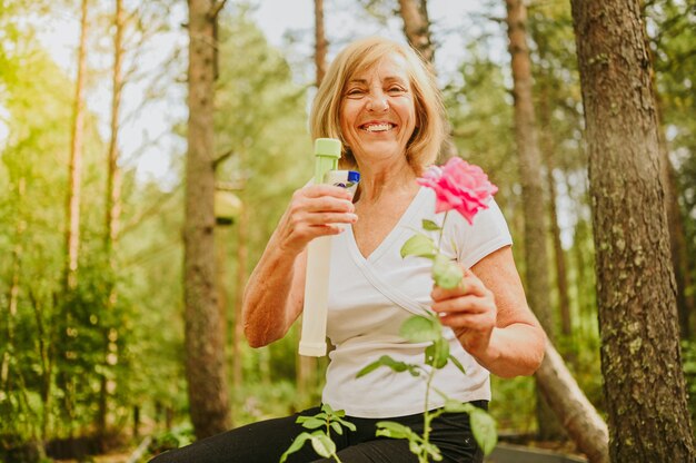 Elderly senior gardener farmer woman caring flowers in summer garden at countryside outdoors sprays