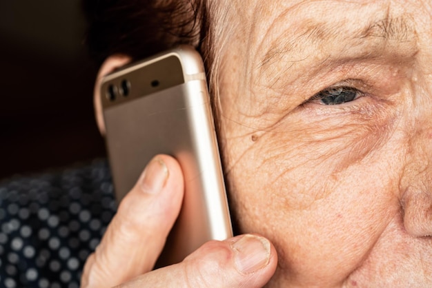 Elderly senior woman holding gold coloured phone next to her ear, closeup detail, only half face visible