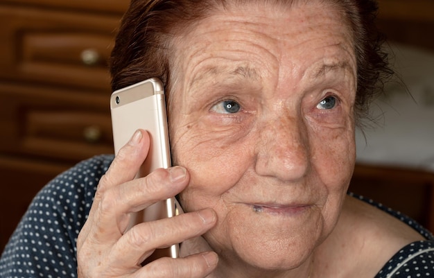 Elderly senior woman holding gold coloured phone next to her ear, closeup detail