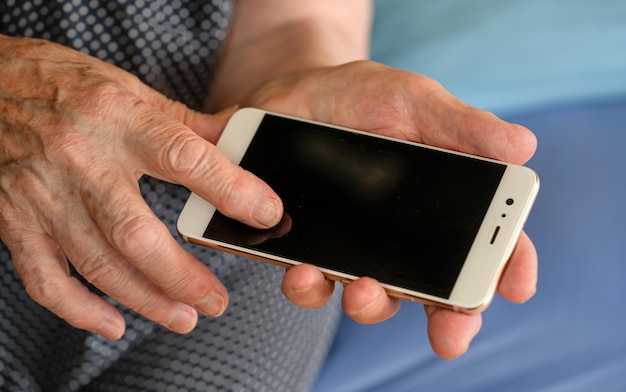 Elderly senior woman holding white mobile phone in her hands, closeup detail