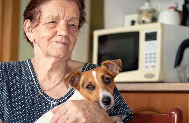 Elderly senior woman posing with her Jack Russell terrier dog in kitchen, focus on person face