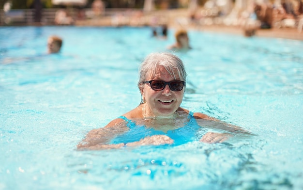 Elderly senior woman with grey hair, wearing blue swimsuit smiling in hotel pool