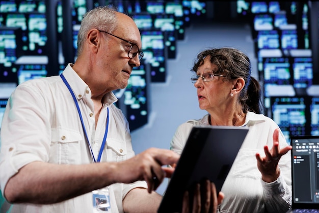 Elderly servicemen running analysis on supercomputers helping businesses manage databases, host websites and store files. Meticulous repairmen auditing high tech server farm electronics