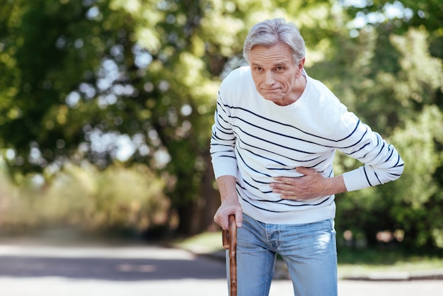 Elderly shocked ill man touching his chest and feeling bad while suffering from stomachache outdoors