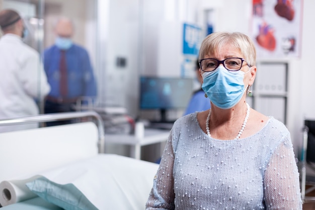 Elderly sick patient with face mask in hospital cabinet waiting for doctor