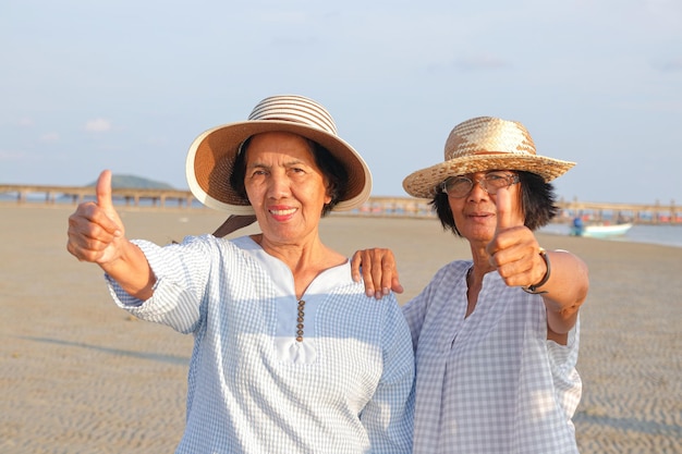 Società anziana in età pensionabile due donne anziane felici di andare al mare e pollice in alto per il gradimento del turismo della pensione