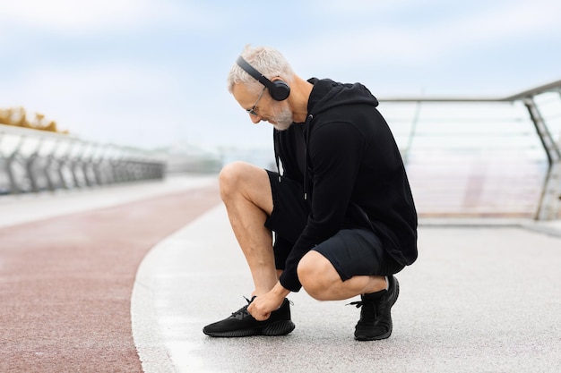 Elderly sportsman tying his shoes before training copy space