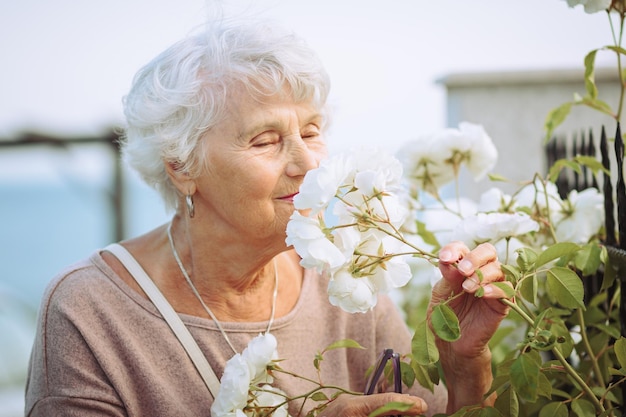 Пожилая женщина любуется красивыми кустами с красочными розами