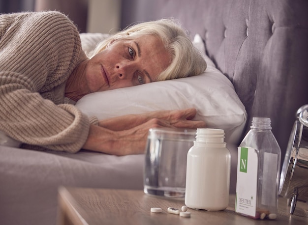 Elderly woman bed and medical addiction with pills medicine or medication while lying awake at home Senior female suffering from sick illness or mental health trauma or disorder in the bedroom