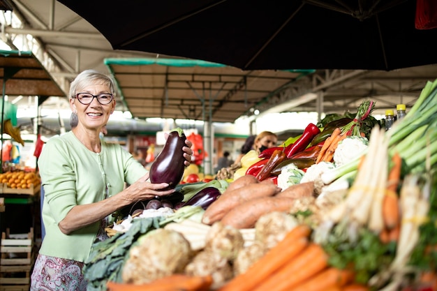 Elderly woman buying vegetables at market place.