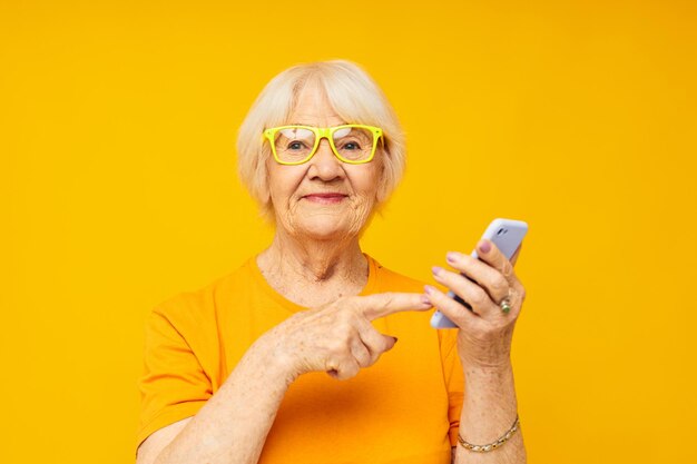 Elderly woman in casual tshirt communication by phone yellow background