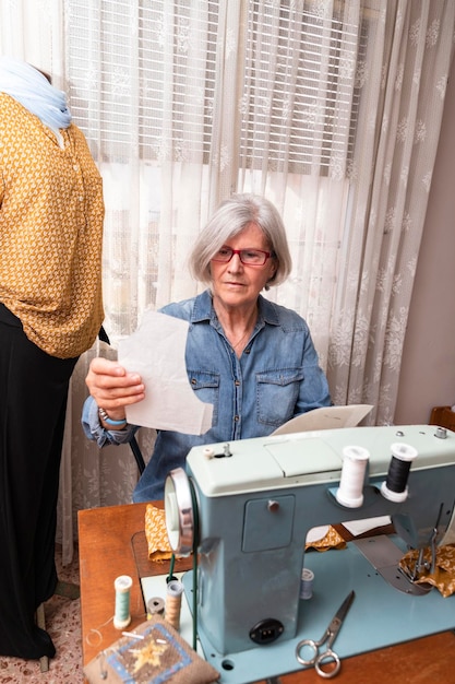 Elderly woman checking a sewing pattern next to a sewing machine