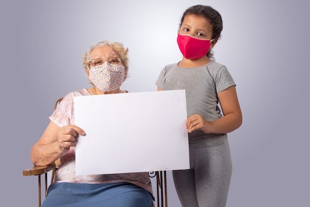 Photo elderly woman and child together in mascara holding a white sign on gray