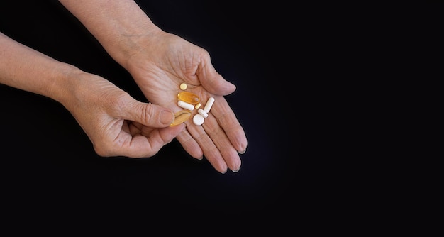 An elderly woman chooses which pill to take hands on a black background