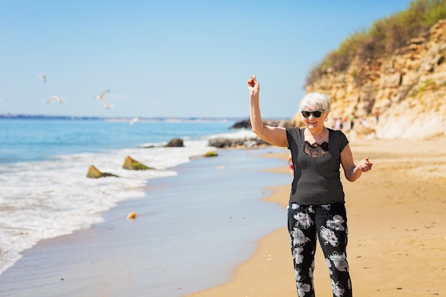 Elderly woman in dark sunglasses feeds seagulls on the beach