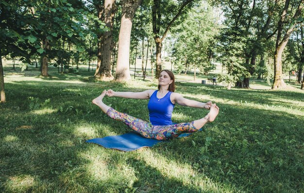 An elderly woman does yoga in the park on a mat Performs complex Asana exercises leads a healthy lif