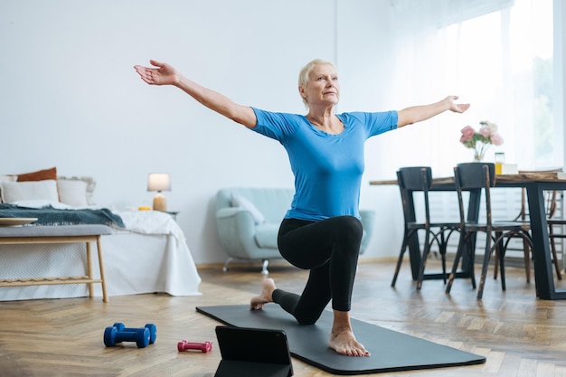 Elderly woman doing exercises with an online trainer in her living room concept of online training