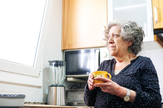 Фото Пожилая женщина пьет чашку кофе на кухне своего дома
