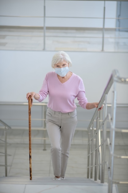 Photo elderly woman in a facial mask going upstairs