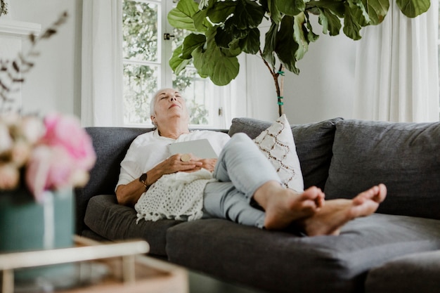 elderly woman fell asleep on a couch with a tablet on her chest