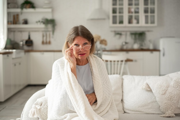 格子縞の眼鏡をかけた年配の女性が自宅のソファで体を温めている