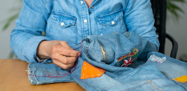 Elderly woman hands sewing on fabric jeans