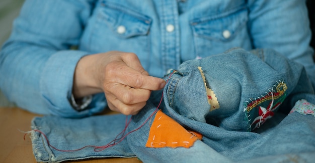Elderly woman hands sewing on a fabric jeans