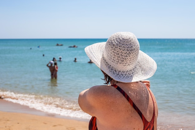 An elderly woman in a hat and swimsuit on the seashore rear view Summer holiday on the coast in retirement