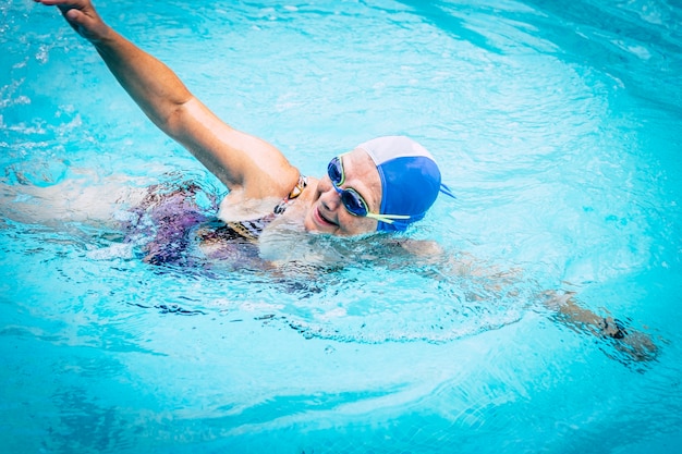 Elderly woman in healthy activity swimming in the outdoor turquoise swimming pool