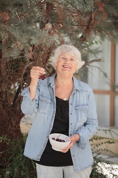 Photo elderly woman holding a bowl of ripe cherries