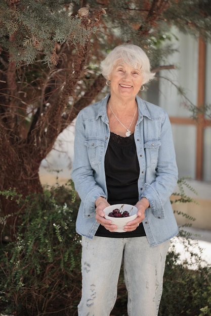 Photo elderly woman holding a bowl of ripe cherries