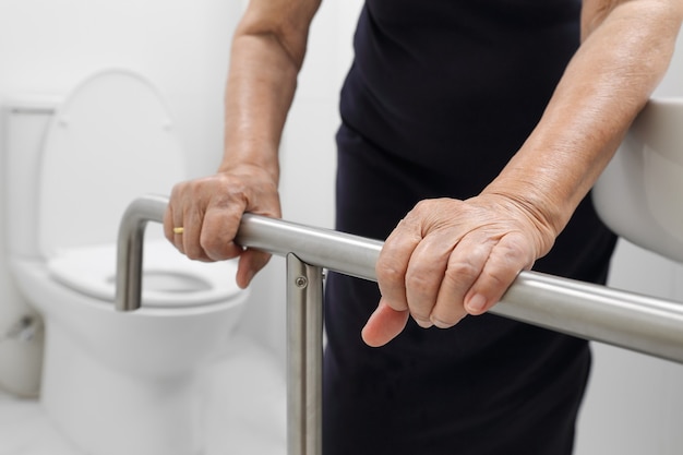 トイレで手すりを握っている年配の女性。