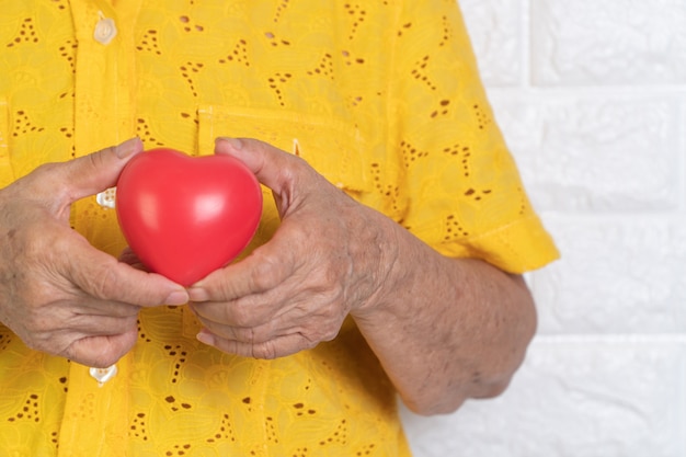 Foto donna anziana che tiene cuore rosso.