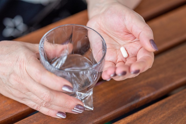 ある年配の女性がコップ一杯の水と薬のカプセルを手に持っています