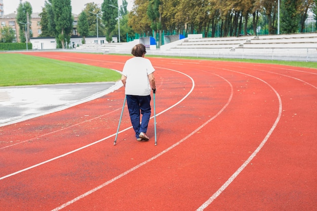 An elderly woman is engaged in walking with sticks in the stadium. Nordic walking