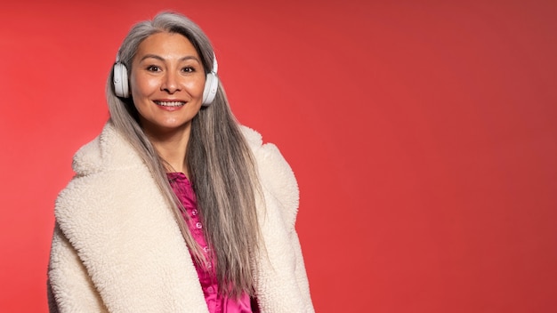 Photo elderly woman listening to music and smiling against a red background