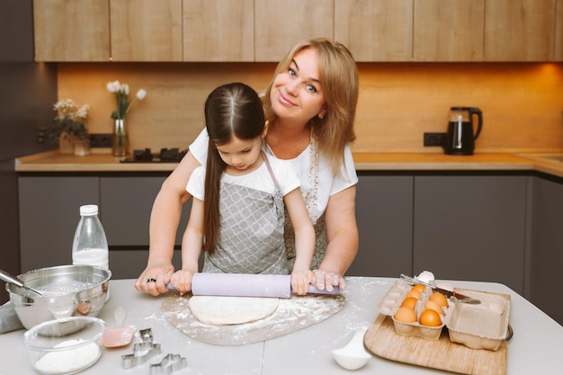 An elderly woman and a little girl roll out soft dough while baking in the kitchen at home grandmother and granddaughter cook cakes