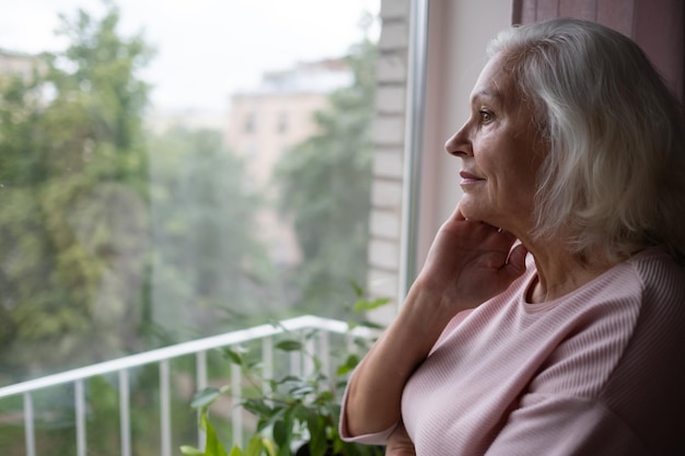 An elderly woman looks sadly out the window