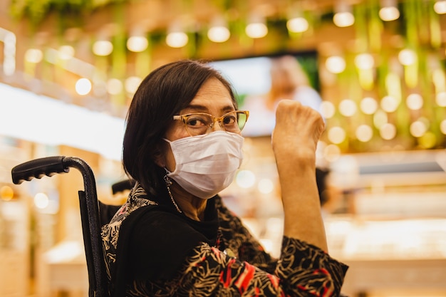 Elderly woman in medical mask sitting in wheelchair wearing eyeglass.