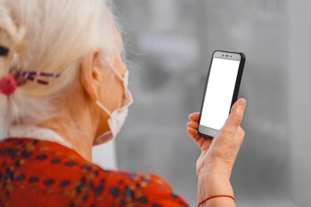 Photo an elderly woman in a medical protective mask looks at the smartphone screen