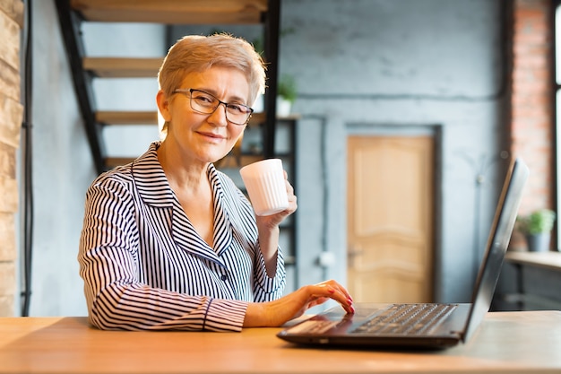 Photo elderly woman in pajamas working on a laptop