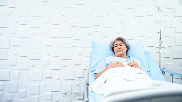 Elderly woman patient lying in bed receiving saline in the patient room have a worried face and weary of her sickness