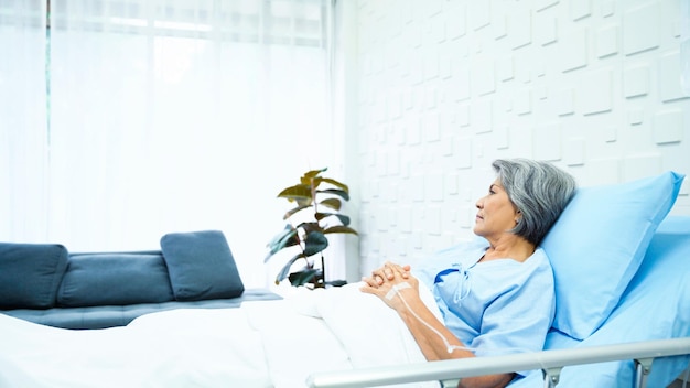 Elderly woman patient lying in bed receiving saline in the patient room have a worried face and weary of her sickness