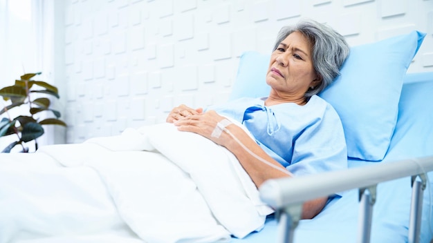 Elderly woman patient lying in bed receiving saline in the patient room have a worried face and weary of her sickness